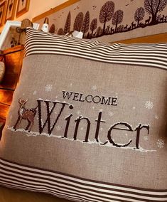 a welcome winter pillow sitting on top of a wooden table next to a stuffed animal