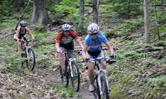 three people riding bikes on a trail in the woods