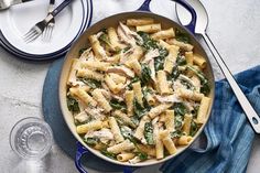 pasta with chicken and spinach in a blue skillet next to silverware on a white surface