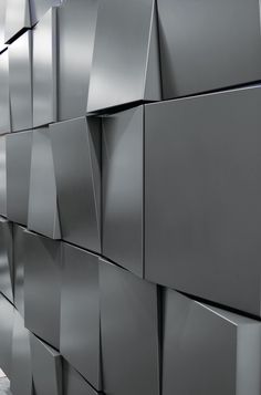 a man walking down a sidewalk next to a wall covered in black cube shaped tiles