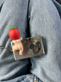 a camera with a red tomato attached to it sitting on someone's lap,