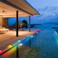 an outdoor swimming pool with colorful lights on the side and water in the back ground