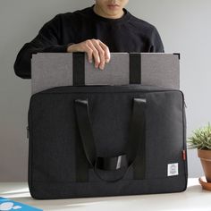 a man holding a laptop bag on top of a white table next to a potted plant