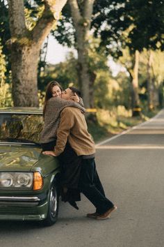 a man and woman leaning on the hood of a green car in front of trees