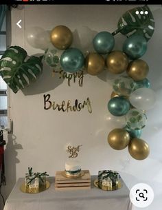 a birthday cake on a table with balloons and greenery in the shape of a wreath