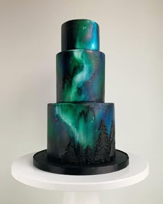 a three tiered cake decorated with an aurora bore and pine trees on the side