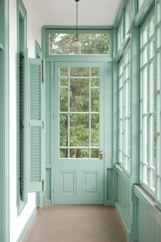 an empty hallway with green painted doors and windows on either side of the door, leading to another room