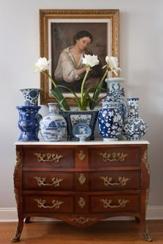 a painting and vases are on top of a dresser in front of a portrait