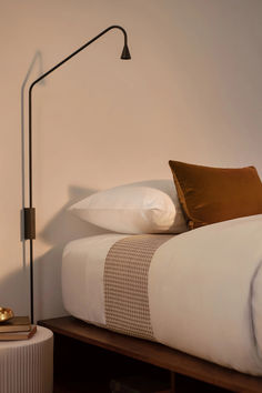 a bed with white sheets, pillows and a floor lamp