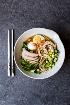 a white bowl filled with noodles, meat and veggies next to chopsticks