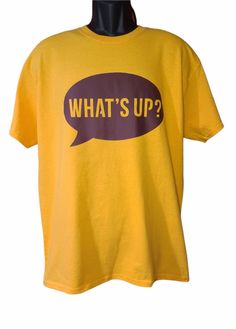 What's Up Graphic Tee  The bright yellow T-shirt features a large, brown speech bubble with the phrase "What's Up" in yellow letters. Add a splash of casual cool to your everyday wardrobe with this What's Up graphic tee! A fun and essential piece for any laid-back ensemble, this tee is perfect for adding a touch of attitude to your look. Upgrade your wardrobe with this must-have item today! trendy shirt, casual style, trendy tee, casual chic, casual graphic tee, everyday wardrobe, what's up tee, Essential Wardrobe Pieces, Essential Wardrobe, Yellow Shirt, Yellow T Shirt, Yellow Shirts, Graphic Apparel, Speech Bubble, Trendy Tee, Trendy Shirts