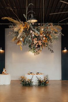 an arrangement of flowers and greenery is hanging from the ceiling above a table with white linens