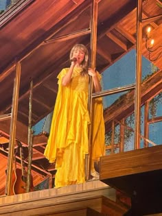 a woman in a yellow dress standing on a stage with her hands to her face