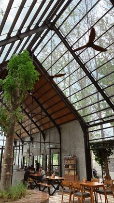 the inside of a restaurant with tables and chairs under a glass roof over looking trees