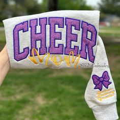 Get cozy and comfortable while showing off your cheer mom pride with this stylish Cheer Mom Sweater. Designed with a cute bow on the sleeve and the option to personalize it with your child's name, this sweater is perfect for cheering on your little one at their next big event. Add a touch of style to your wardrobe and show your support - grab your Cheer Mom Sweater today! Loose-Fitting: Provides maximum comfort and movement during cheer practice or competitions. Long Sleeve: Keeps you warm during chilly days, while the lightweight feature makes it perfect for layering. Cute & Elegant Style: The embroidered pattern adds a chic and retro touch to your casual outfit, while the cute bow embellishment makes it perfect for any occasion. This Cheer Mom Sweater is not only stylish but also functio Cheer Mom Sweatshirt Ideas, Cheer Sweatshirts, Cheer Mom Sweatshirt, Customizable Cotton Sweatshirt For Cheerleading, Customizable Long Sleeve Cheerleading Sweatshirt, Crew Neck T-shirt With Name Print For Cheerleading, Sweater Embroidery, Grandparents Shirt, Cheerleading Shirts