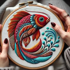 two hands are holding a colorful fish embroidery