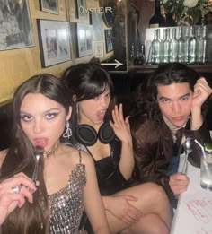 three people sitting at a table with headphones on their ears and one person holding a drink