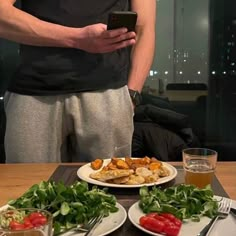 a man standing at a table with plates of food on it and cell phone in his hand