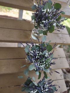 two vases with flowers hanging from the side of a wooden bench next to each other