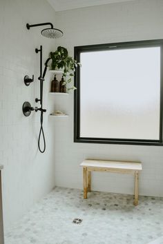 a white tiled bathroom with a window and bench next to it, in front of the shower