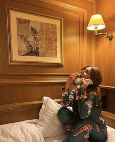 a woman sitting on top of a bed talking on a cell phone while wearing pajamas