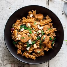 a black bowl filled with pasta and spinach on top of a white wooden table