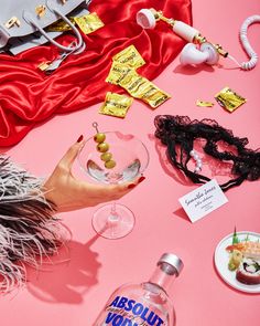 a woman holding a wine glass next to several other items on a pink tablecloth