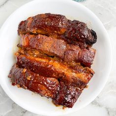 ribs covered in bbq sauce on a white plate next to bowls of coleslaw