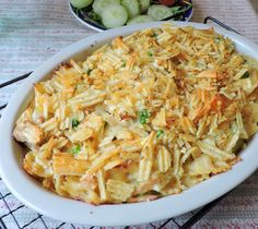 a white dish filled with pasta and vegetables next to a bowl of cucumbers