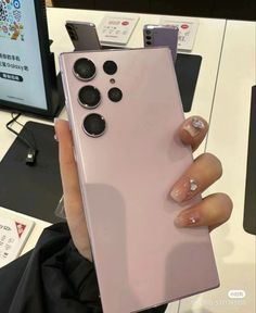 a person holding up a pink phone in front of a computer desk with other electronics on it