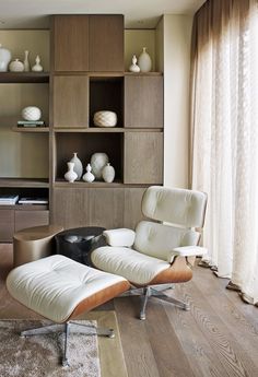 a living room with a chair and ottoman next to a book shelf filled with vases