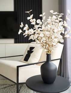 a black vase with white flowers sitting on a table in front of a couch and television