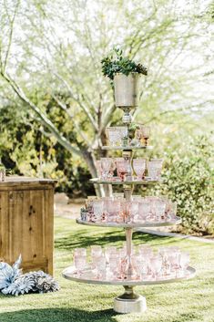 a tiered cake stand with cups on it in the middle of a lawn area