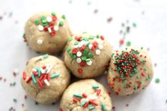 four cookies with sprinkles and colored candies on top are arranged next to each other