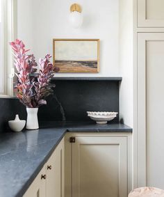 a vase with some purple flowers in it on a counter top next to a window