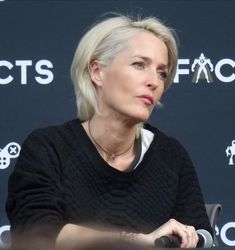 a woman sitting at a table in front of a black wall with white writing on it