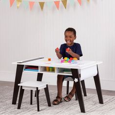 a young boy sitting at a table with toys in front of him and smiling for the camera