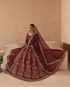 a woman in a red and gold bridal gown sitting on steps with her hands behind her head