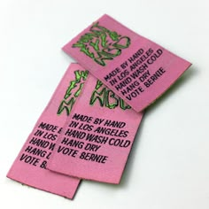 two pink tags with green writing on them