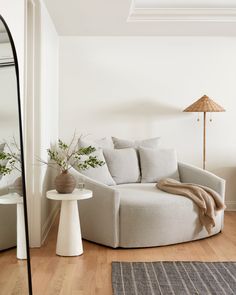 a white couch sitting on top of a hard wood floor next to a mirror and table