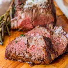 two pieces of steak sitting on top of a wooden cutting board