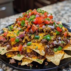 a black plate topped with nachos covered in cheese and toppings on top of it