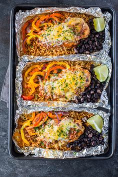 three chicken enchiladas on tin foil with black beans and lime wedges