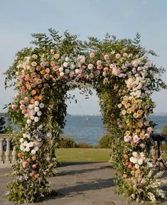 an outdoor wedding arch with flowers and greenery on the top, overlooking the water