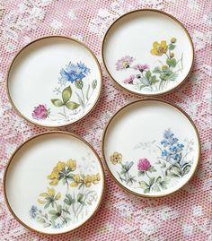 four plates with flowers painted on them sitting on a pink tableclothed surface,