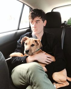 a young man sitting in the back seat of a car holding a large brown dog