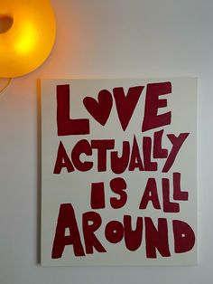 a red and white poster with the words love actually is all around on it next to a yellow lamp