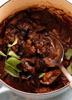 a pot filled with meat and vegetables on top of a table next to a spoon