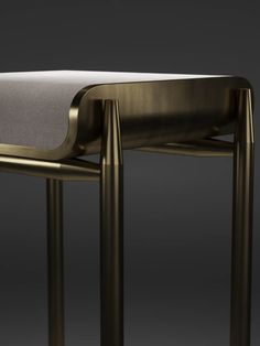 a gold metal stool with a white cushion on the seat and backrest, in front of a dark background