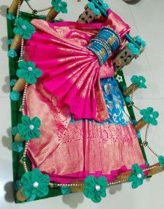 a pink and blue sari with green flowers on the border, sitting on top of a